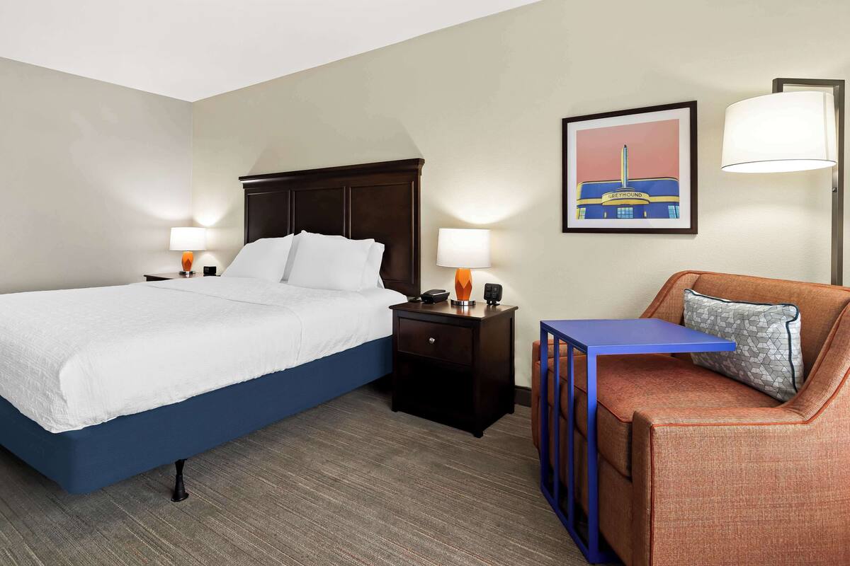 A hotel room with a bed, nightstands, a desk, a chair, and a framed picture on the wall.
