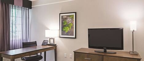 A hotel room with a desk, chair, television, and a cabinet.