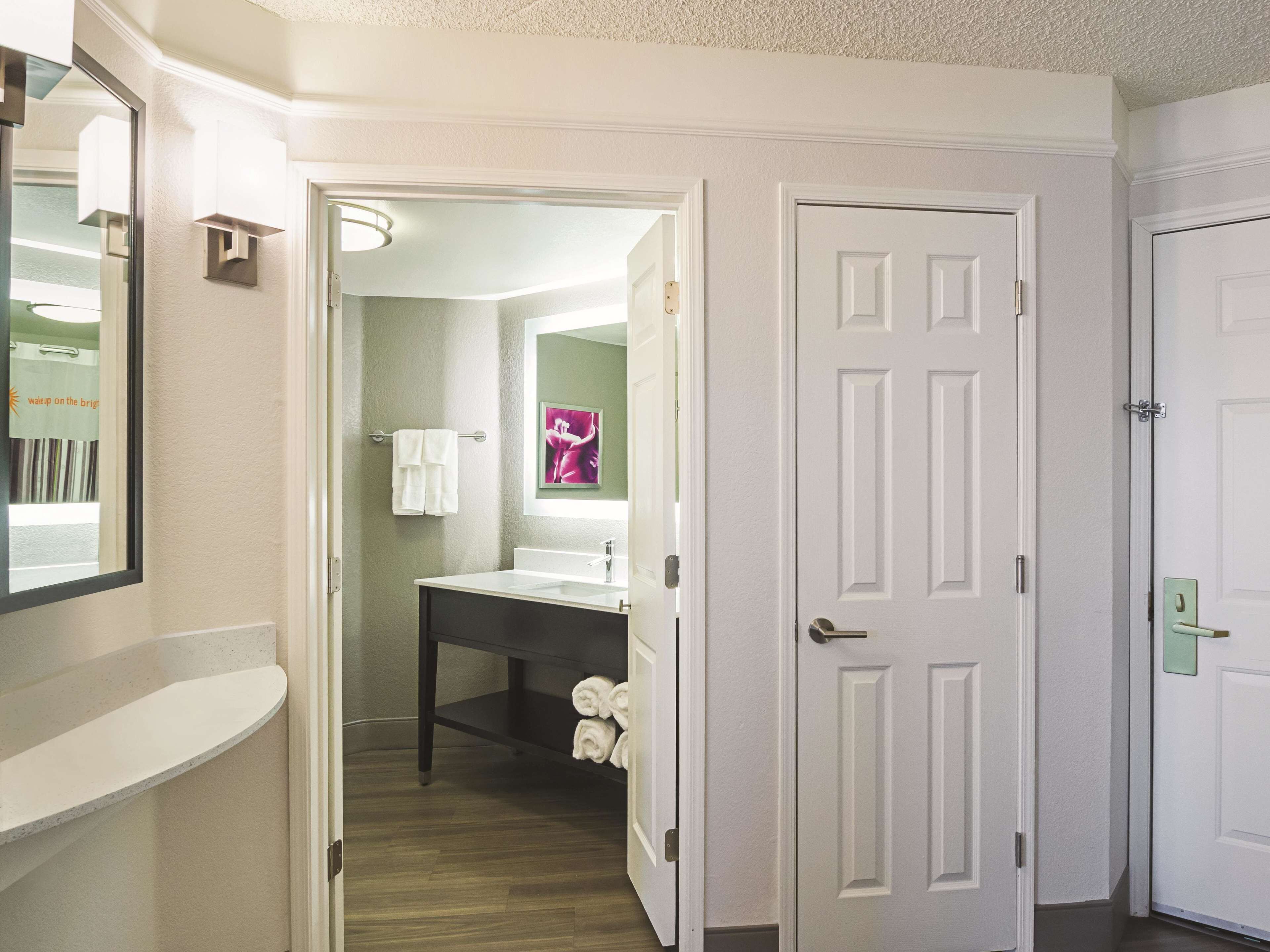 A hallway leading to a bathroom with a white door, a mirror, and a towel rack with towels.