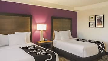Habitación de hotel con dos camas, una mesita de noche con lámpara y una pared decorada con cuadros.