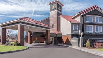 A hotel entrance with a covered parking area, a prominent tower with the hotel name, and a two-story building with a red-tiled roof.