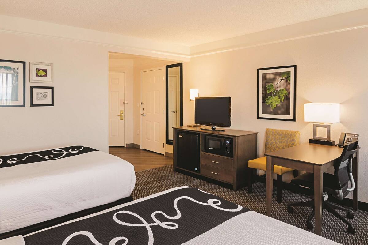 A hotel room with a bed, a desk with a lamp, a TV, a microwave, and a chair.