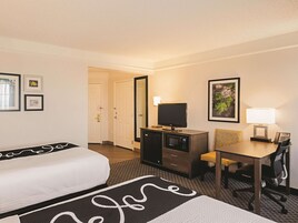 A hotel room with a bed, a desk with a lamp, a TV, a microwave, and a chair.