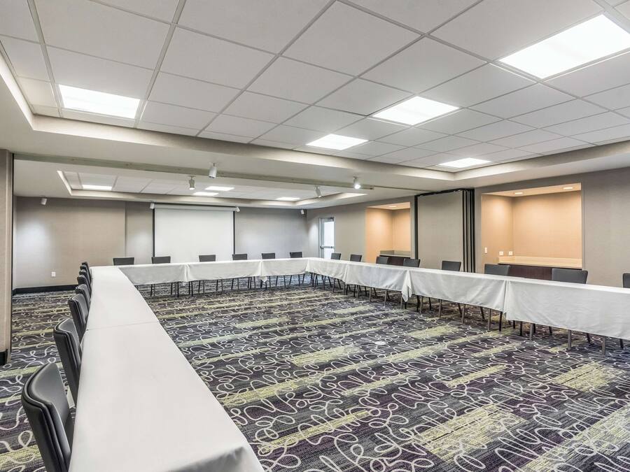 A conference room with a long table, chairs, carpeted floor, and a projector screen.
