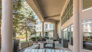 An outdoor patio area with wicker furniture and a striped sofa, large windows, and a view of a multi-story building. - La Quinta Inn & Suites by Wyndham Denver Tech Center (Greenwood Village)
