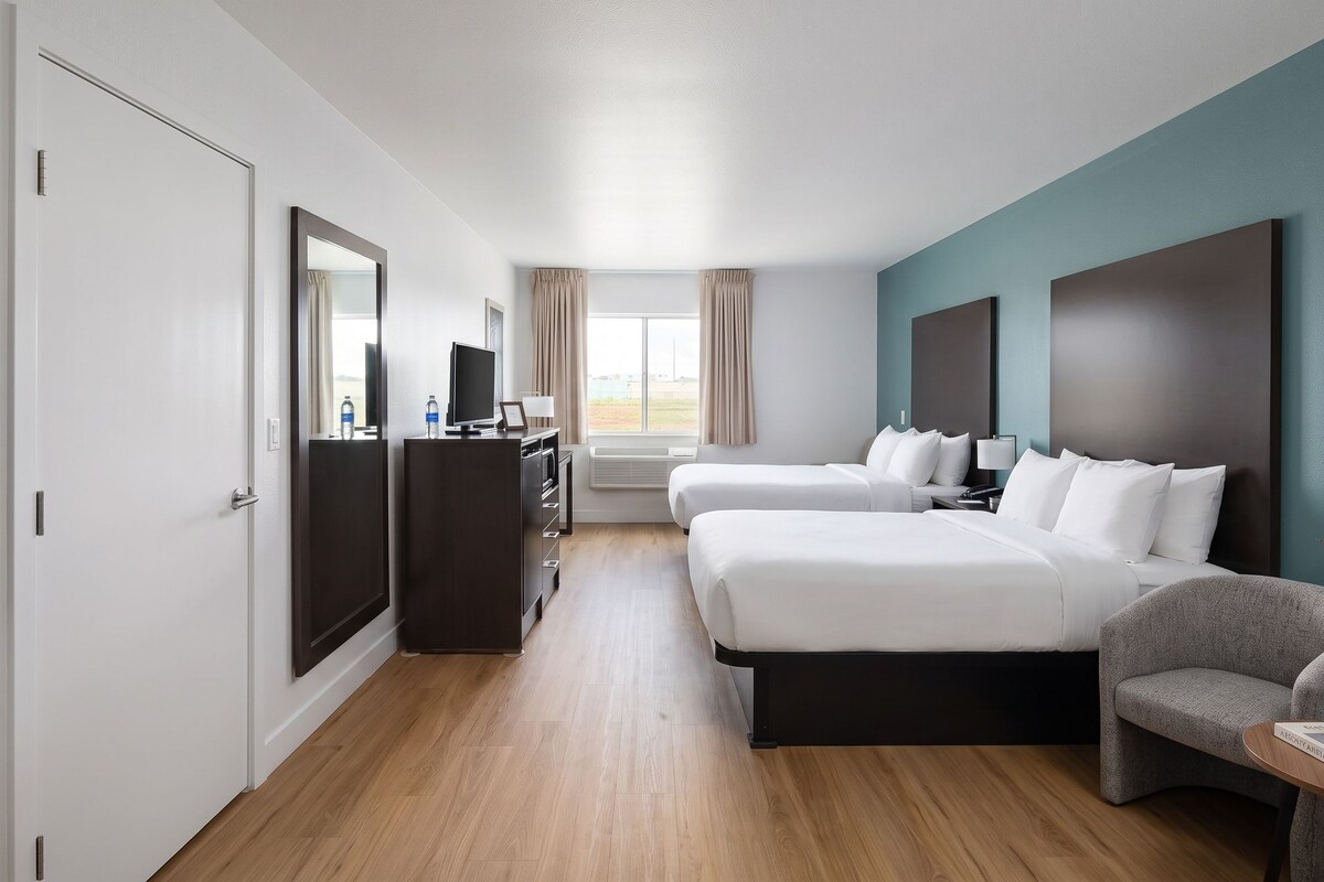 A hotel room with two beds, a desk, a chair, and a window with curtains.