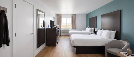 A hotel room with two beds, a desk, a chair, and a window with curtains.