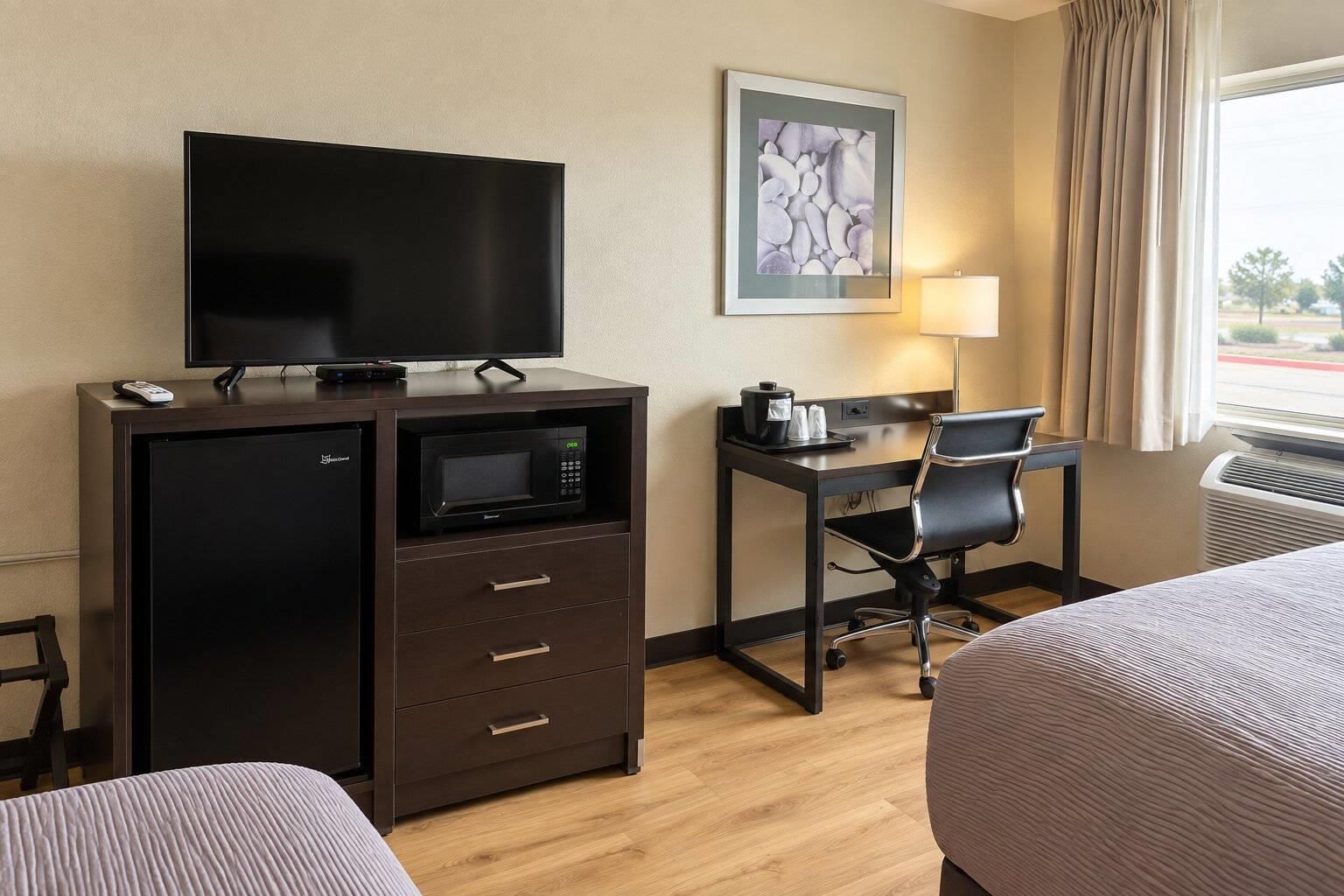 Quarto de hotel com televisão de tela plana, micro-ondas, escrivaninha e duas camas.