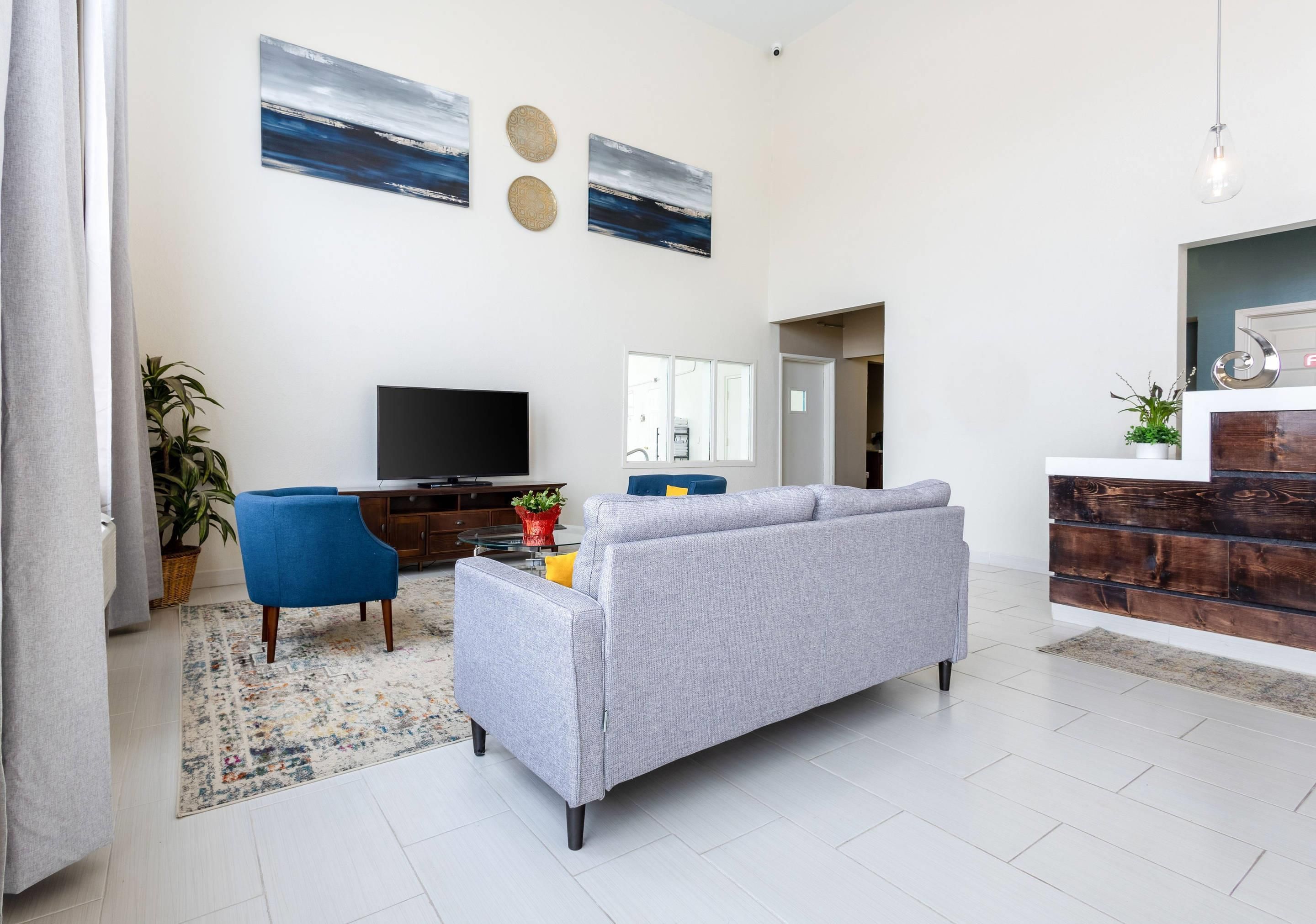 A modern living room with a grey sofa, a blue armchair, a flat-screen TV, and a decorative wall with two circular patterns.