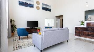 A modern living room with a grey sofa, a blue armchair, a flat-screen TV, and a decorative wall with two circular patterns.
