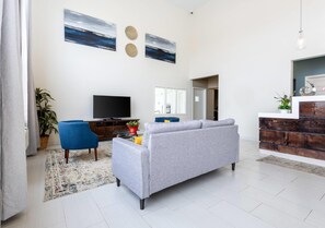 A modern living room with a grey sofa, a blue armchair, a flat-screen TV, and a decorative wall with two circular patterns. - Quality Inn Winslow I-40 (Winslow)