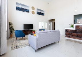 Una sala moderna con un sofá gris, un sillón azul, un televisor de pantalla plana y una pared decorativa con dos diseños circulares.
