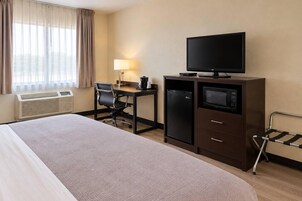 Habitación de hotel con cama, escritorio, silla, televisión, refrigerador y microondas, y ventana con cortinas.