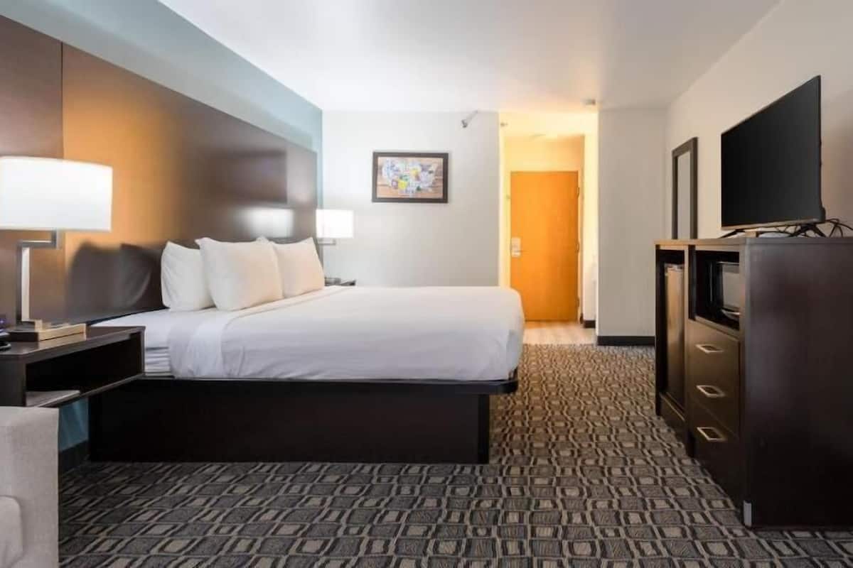 A hotel room with a bed, a desk with a lamp, a TV, and a wardrobe.