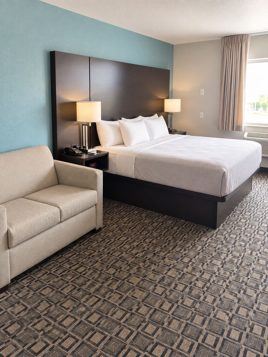 Quarto de hotel com cama, sofá, mesa de cabeceira com abajur e aquecedor fixado na parede.