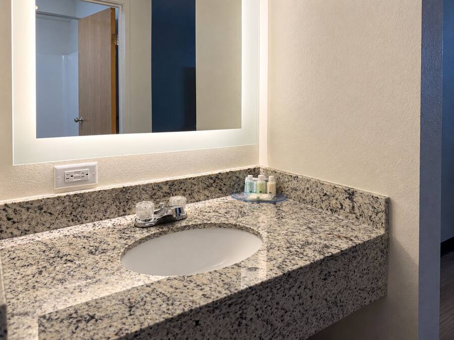 A bathroom with a granite countertop, a sink, and a mirror. There are toiletries on the countertop.
