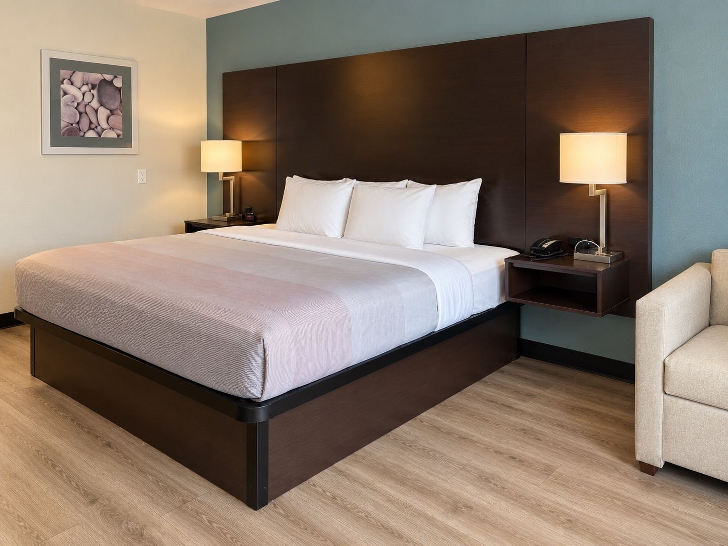 Habitación de hotel con una cama grande, dos mesitas de noche con lámparas, una silla e imagen enmarcada en la pared.