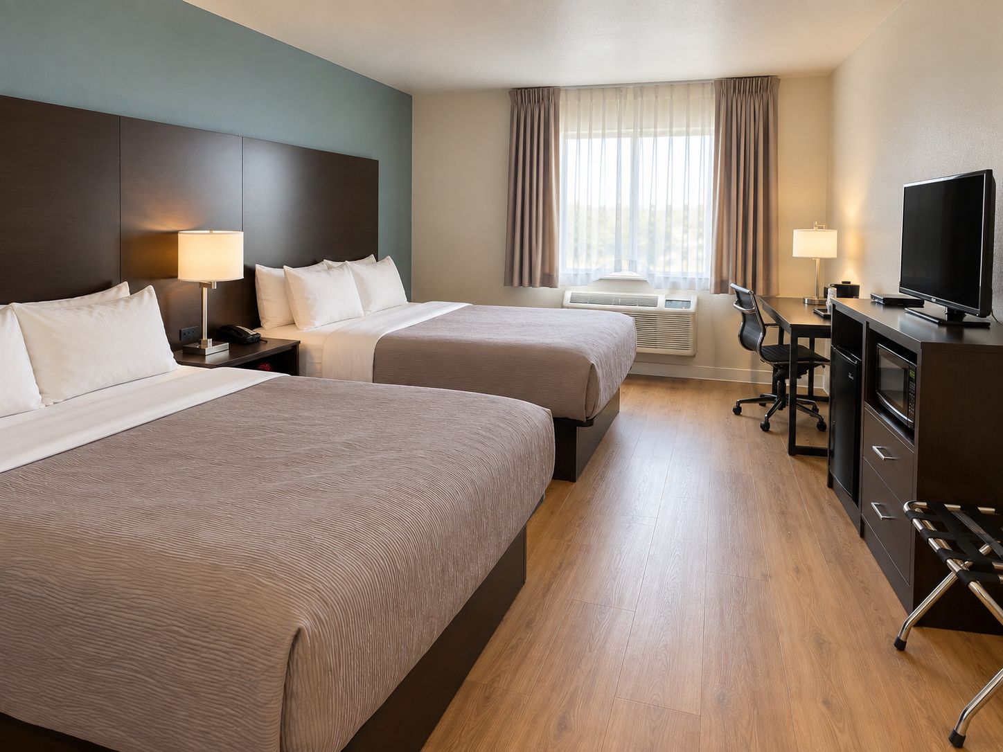 Et hotelværelse med to senge, et skrivebord med tv, en stol og en skrivebordslampe.