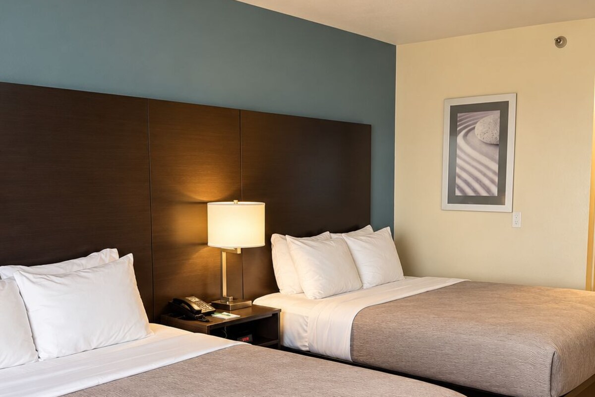 Una habitación de hotel con dos camas, una mesita de noche con una lámpara y un cuadro en la pared.