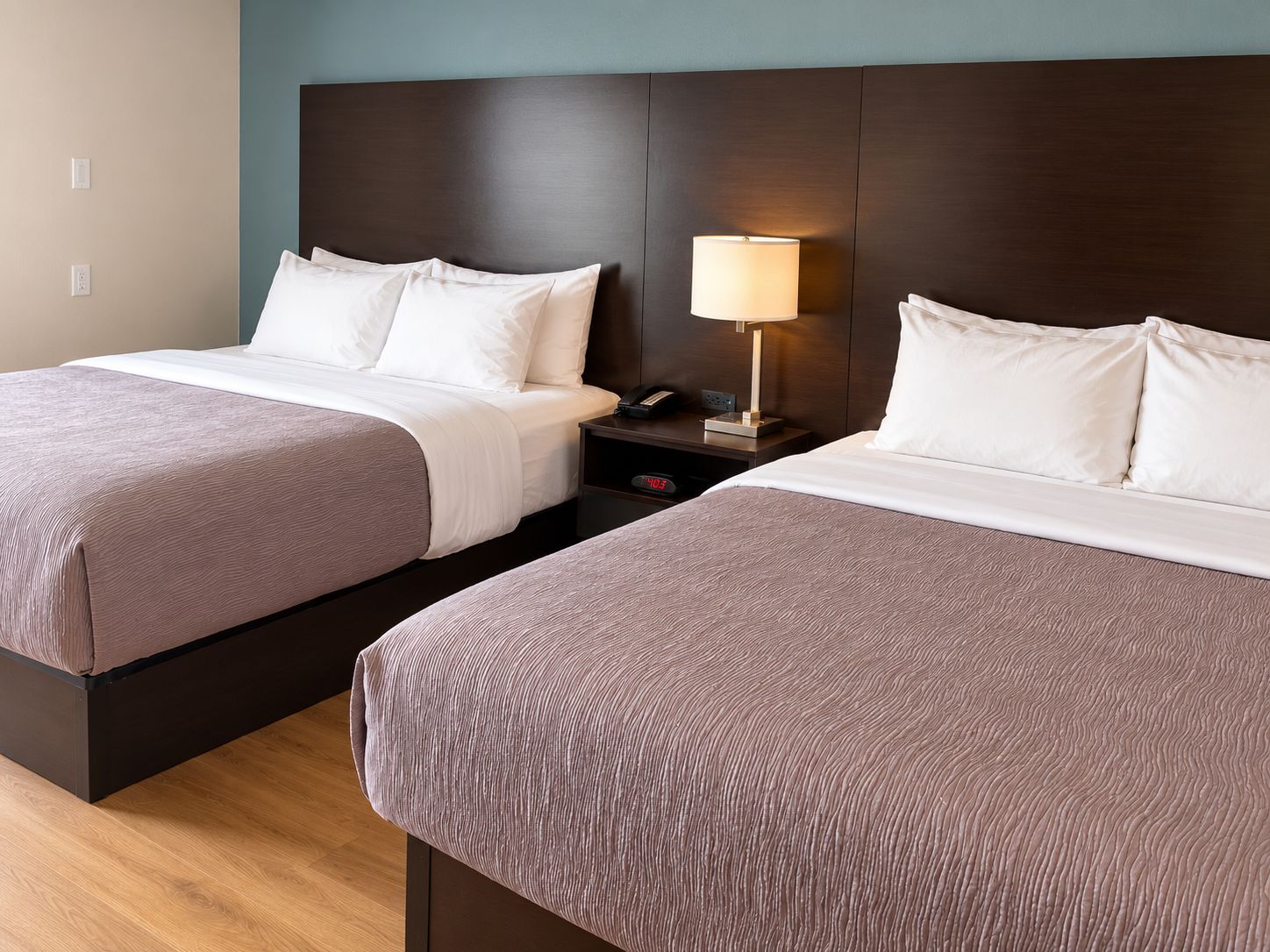 Una habitación de hotel con dos camas, una mesita de noche con lámpara y un reloj digital.