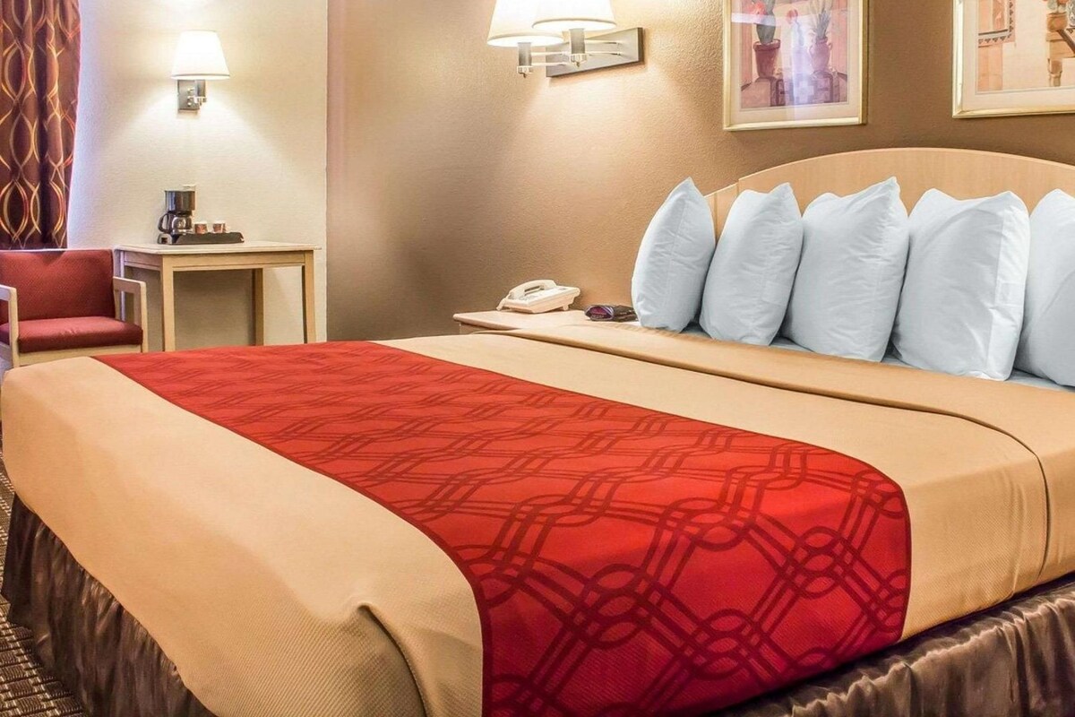 A hotel room with a large bed, a desk with a phone, a chair, and a lamp.