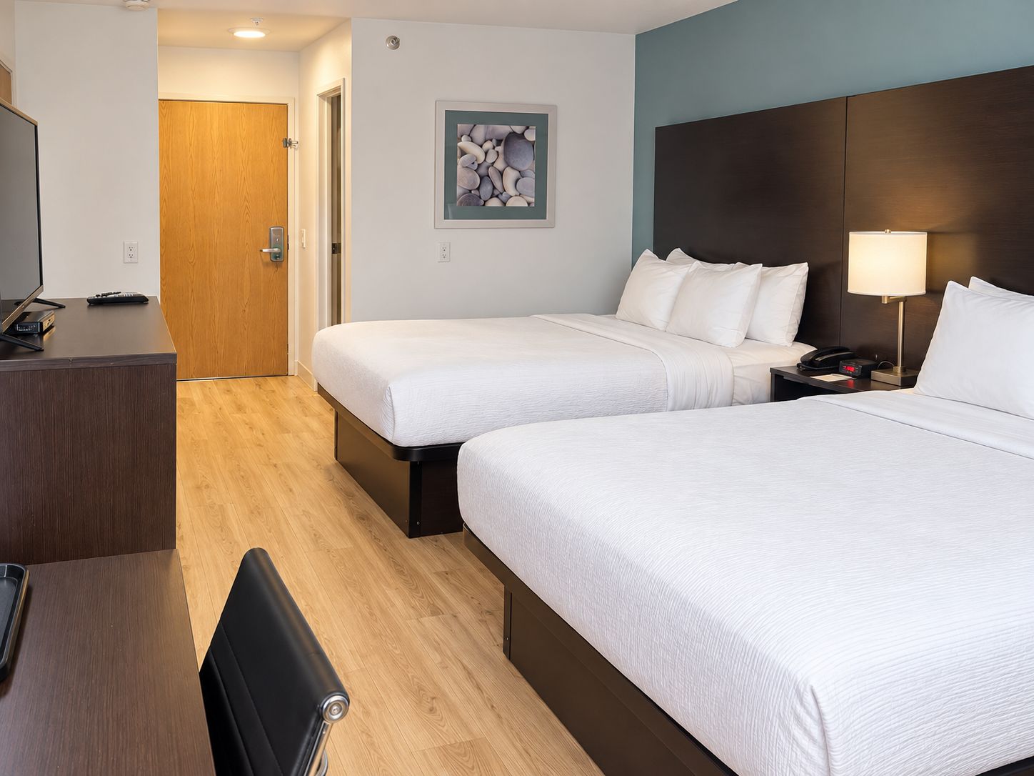 Ein Hotelzimmer mit zwei Betten, einem Schreibtisch mit Fernseher und einer Tür zu einem weiteren Raum.