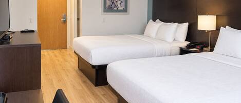 A hotel room with two beds, a desk with a television, and a door leading to another room.