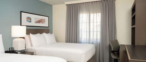 A hotel room with two beds, a desk, a chair, a lamp, and a framed picture on the wall.