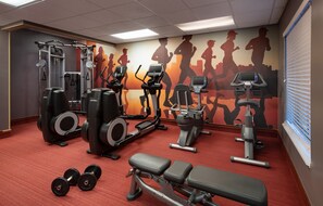 Un gimnasio con varios equipos de ejercicio, como cintas de correr, máquinas de pesas y mancuernas.