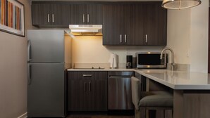 A modern kitchen with dark wood cabinets, stainless steel appliances, and a bar stool. - HYATT house Denver Tech Center (Greenwood Village)