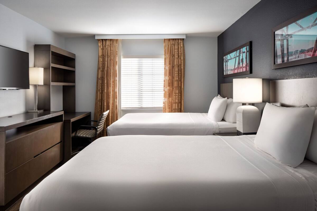 A hotel room with two beds, a desk, a chair, a TV, and a window with curtains.