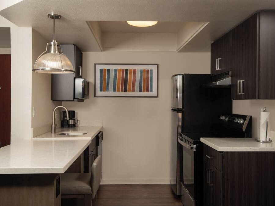 A modern kitchen with dark wood cabinets, a stainless steel refrigerator, and a pendant light.