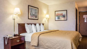 A hotel room with a large bed, two bedside lamps, a nightstand with a phone, and two framed pictures on the wall.