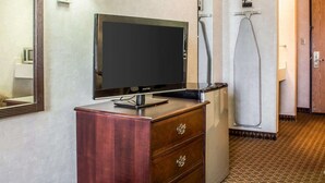 A hotel room with a flat-screen TV on a wooden dresser, a wall-mounted lamp, a mirror, a shower, and a door leading to another room. - Quality Inn & Suites Yuma (Yuma)