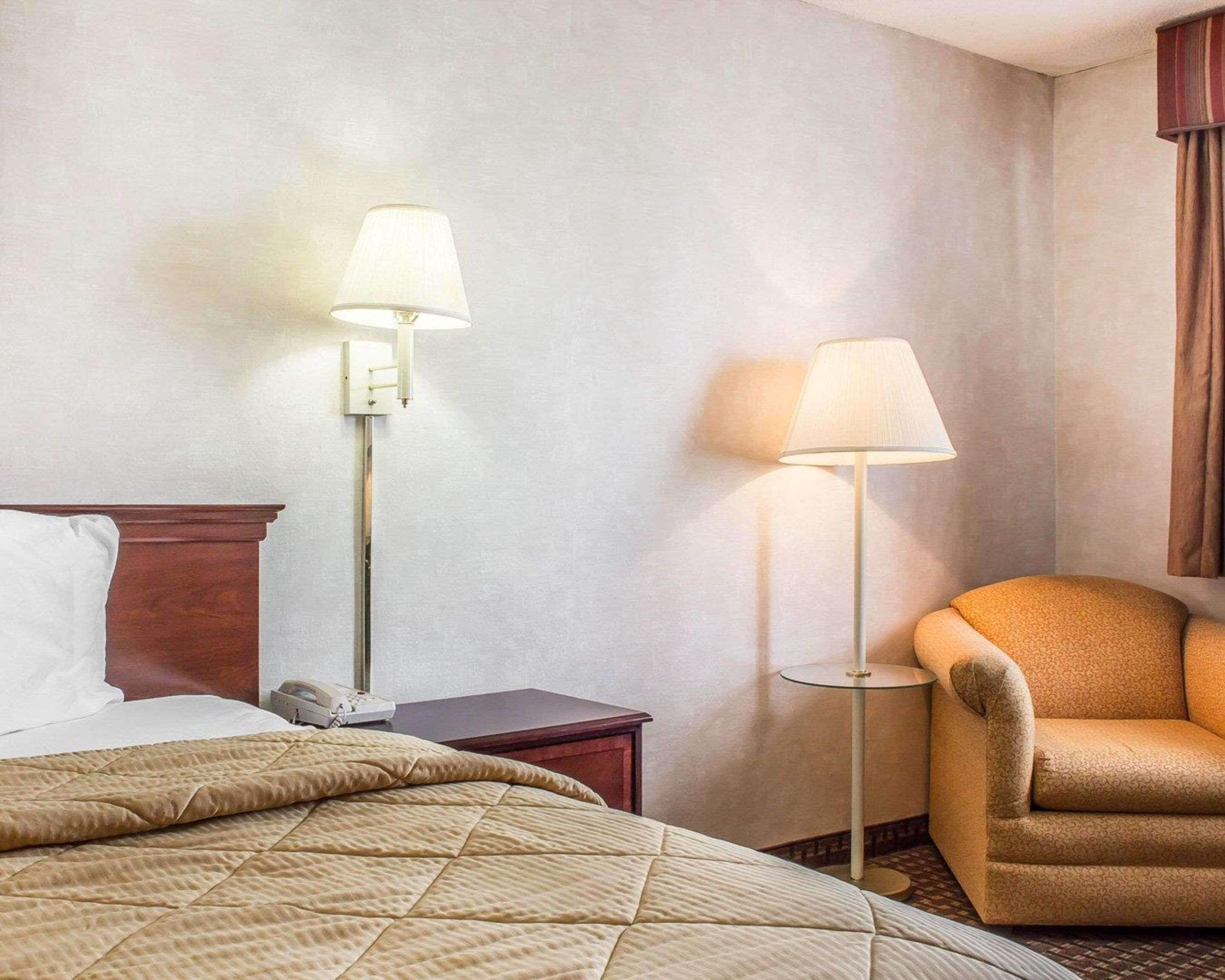 A hotel room with a bed, two bedside lamps, a chair, and a small table.