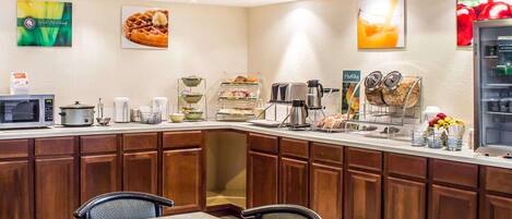 A hotel kitchen with a buffet setup, including a microwave, coffee maker, and various food items.