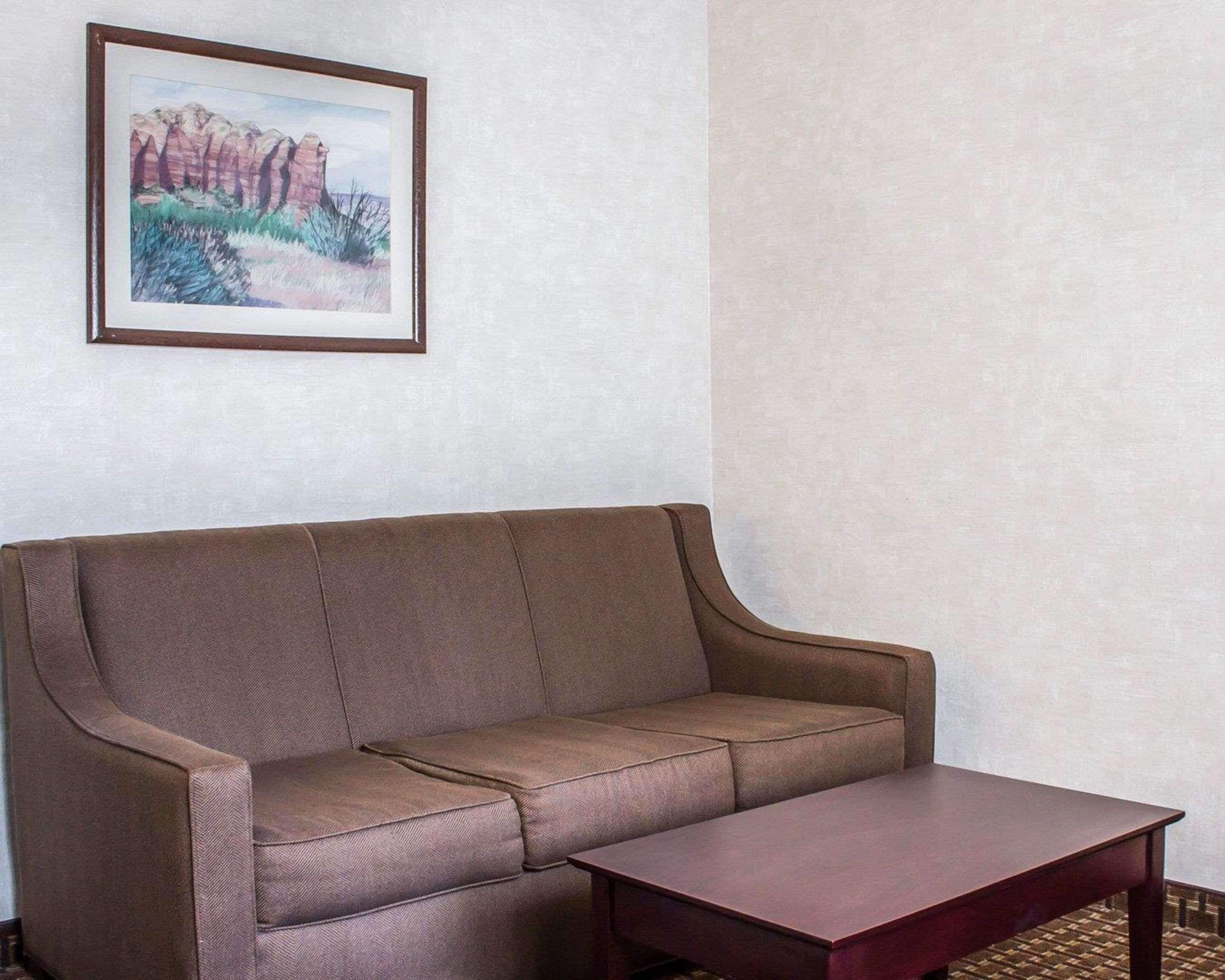 A brown sofa and a wooden coffee table in a room with a plain white wall and a framed painting of a landscape.