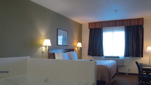 A hotel room with a large bathtub, a bed with two pillows, a desk, and a chair. - Quality Inn & Suites Yuma (Yuma)