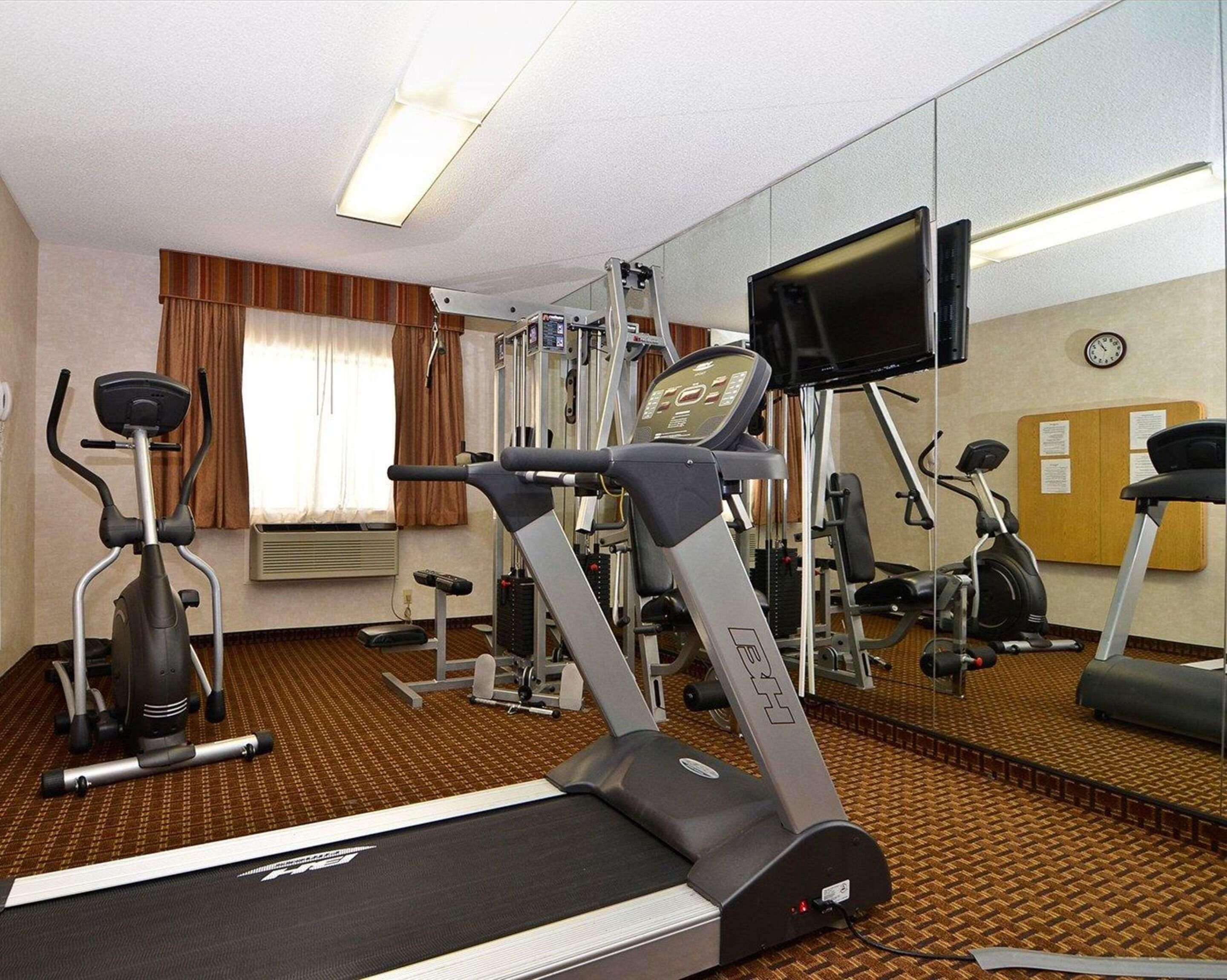 A hotel gym with cardio machines, a mirror, and a clock on the wall.