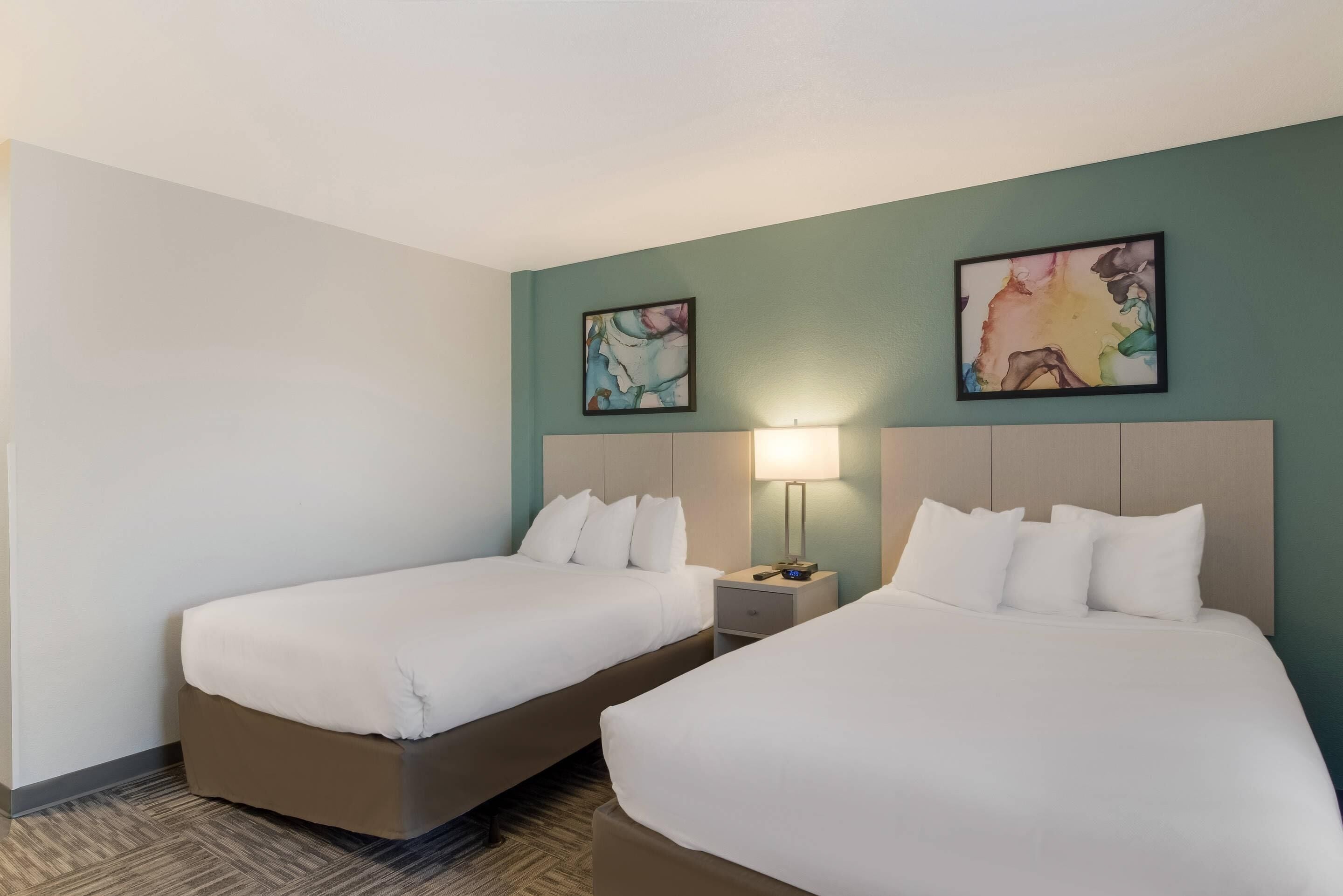 Een hotelkamer met twee bedden, een nachtkastje met een lamp en abstracte wanddecoratie.