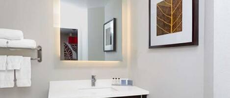 A modern bathroom with a white sink, dark-toned cabinet, and a framed artwork on the wall.