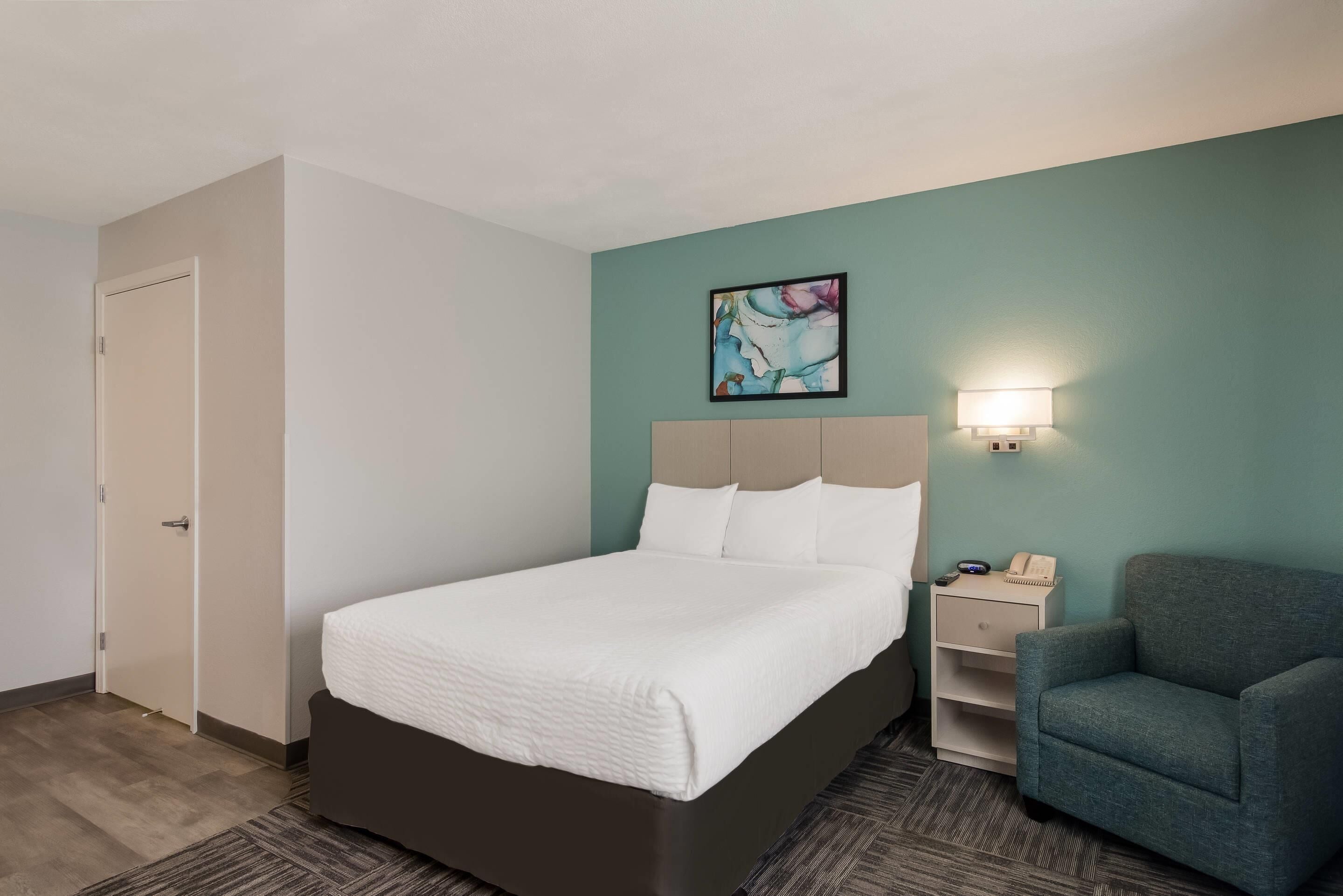 Une chambre d’hôtel avec un lit, une chaise, une table de chevet et un tableau au mur.