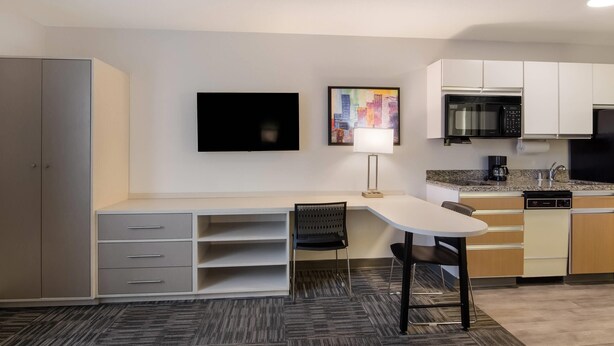A compact kitchen with a microwave, stove, and sink. There is a dining table with chairs and a TV mounted on the wall. - MainStay Suites Denver Tech Center (Centennial)