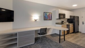 A modern kitchen with a flat-screen TV, a dining area with a chair, and a microwave. - MainStay Suites Denver Tech Center (Centennial)