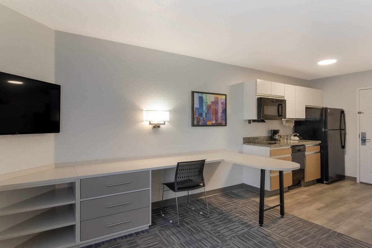 A modern kitchen with a flat-screen TV, a painting, and a refrigerator.