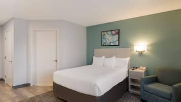 A hotel room with a bed, a nightstand, a chair, and a painting on the wall.
