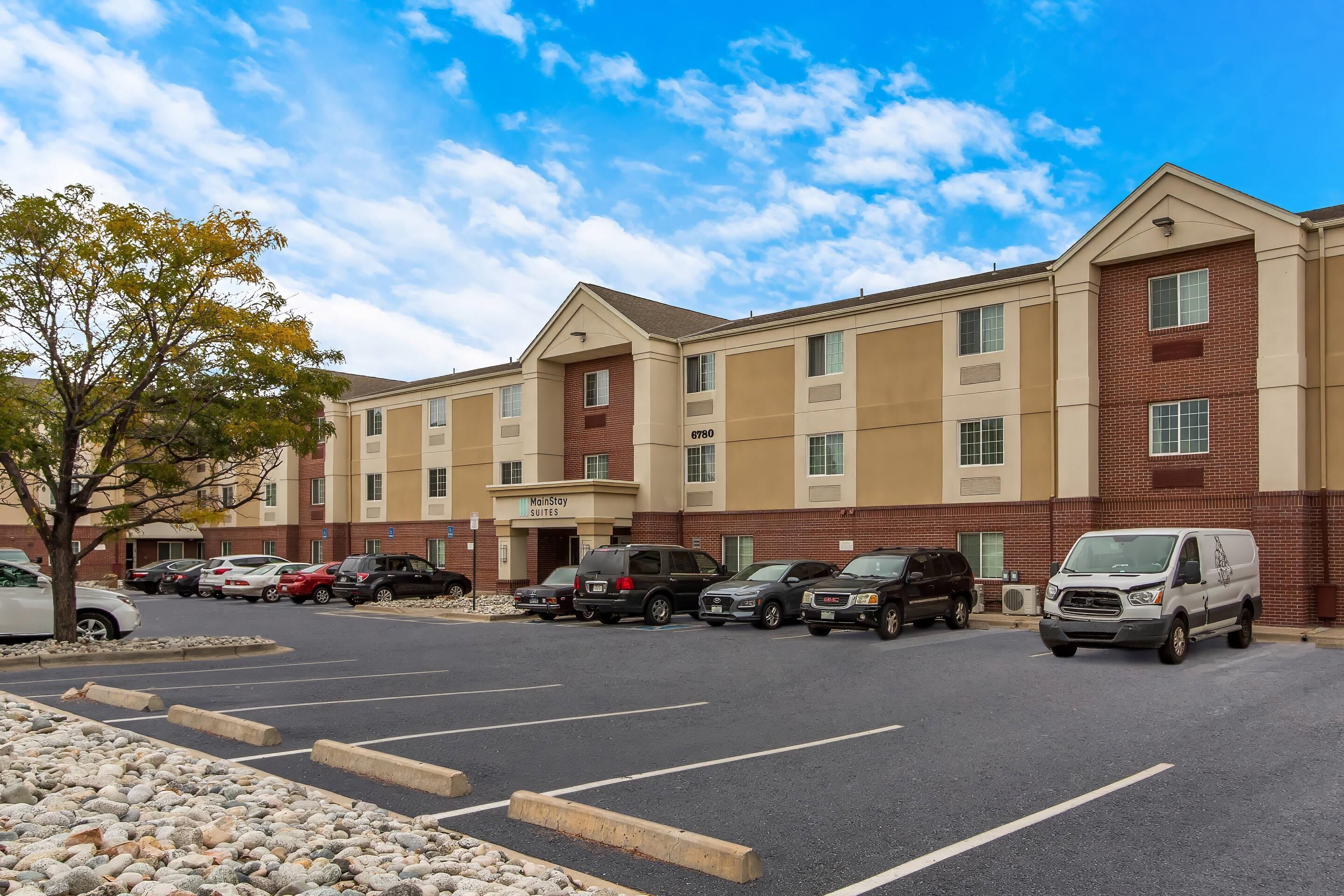 A hotel with a parking lot, a tree, and a clear sky.