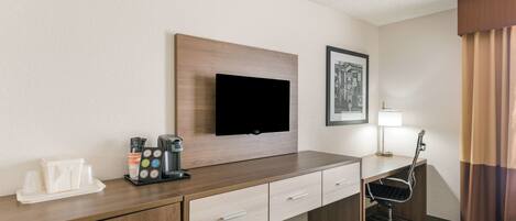 Habitación de hotel con escritorio de madera, televisor de pantalla plana en la pared, un cuadro enmarcado, una lámpara y una silla.