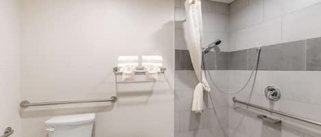 Un baño con inodoro, ducha con puerta de vidrio y barra de apoyo.