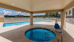 A covered swimming pool with a hot tub, lounge chairs, and a view of a mountain and trees.